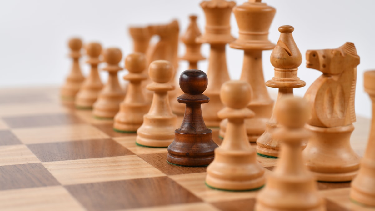 Single dark chess pawn standing among light pieces on a wooden board representing being repositioned during organizational change